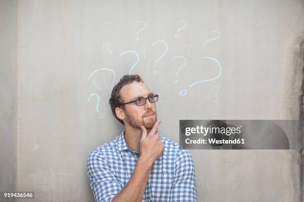 man standing next to a concrete wall with chalk question mark drawings - vragen stockfoto's en -beelden