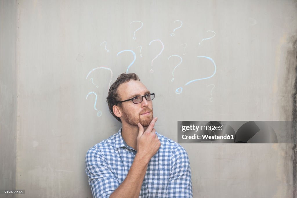 Man standing next to a concrete wall with chalk question mark drawings