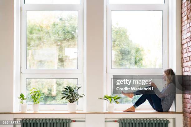 woman sitting at home on the window sill, drinking coffee - window sill stockfoto's en -beelden