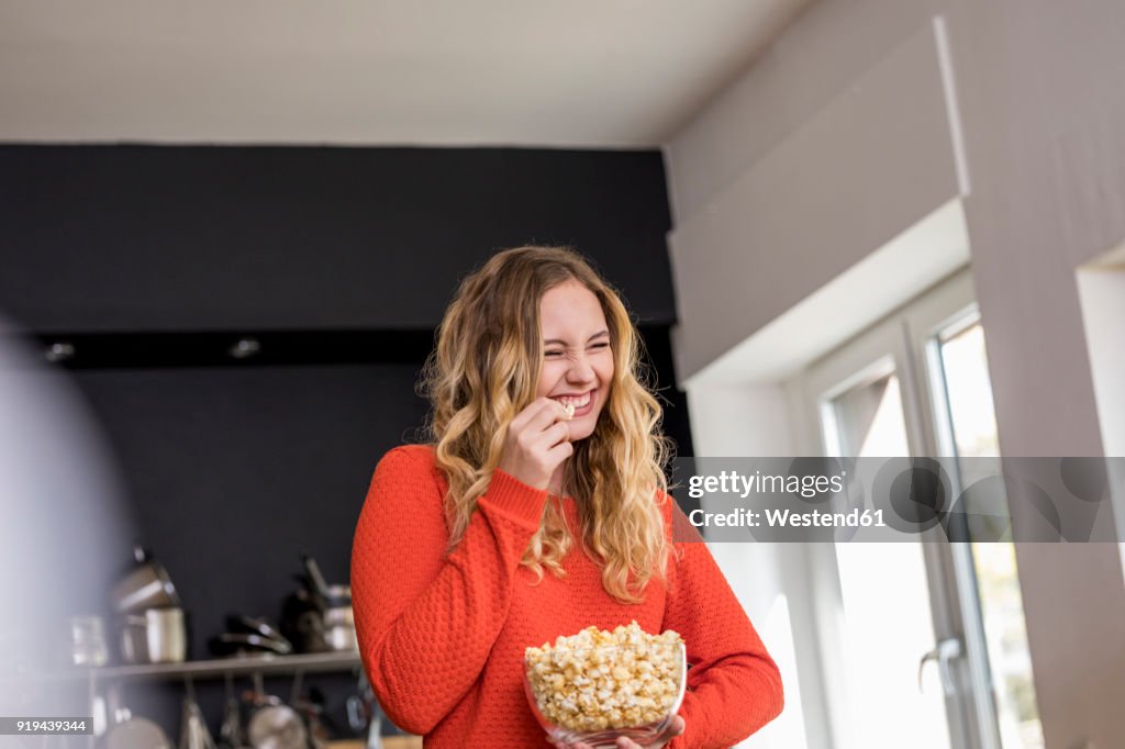 Portrait of giggling young woman with bowl of popcorn in the kitchen