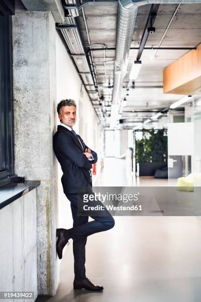 portrait of confident mature businessman standing in office - leaning ストックフォトと画像