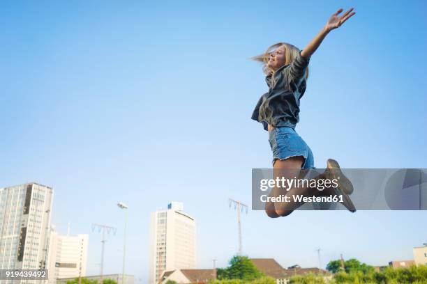 happy young woman jumping in the air - women in daisy dukes stock-fotos und bilder