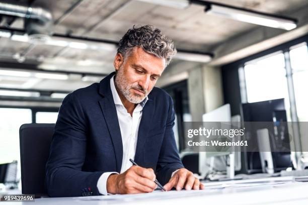 mature businessman writing at desk in office - business person writing stock pictures, royalty-free photos & images