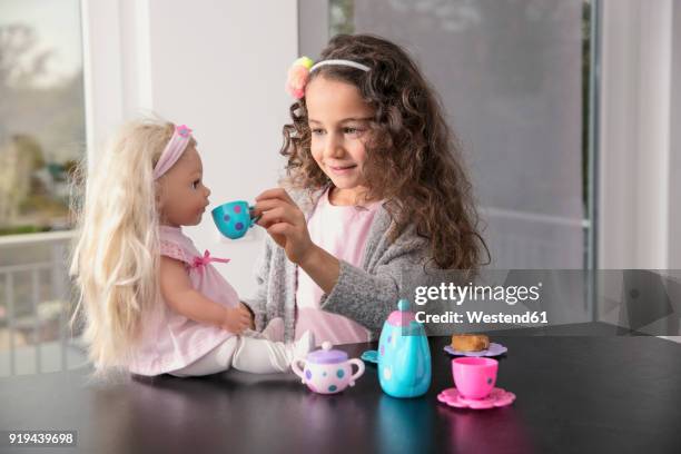 portrait of smiling little girl playing with doll and doll's china set - bambola giocattolo foto e immagini stock