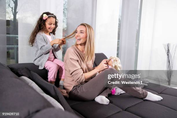 little girl braiding her mother's hair on the couch - braided hair photos et images de collection