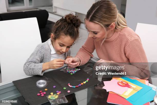 mother and little daughter stringing beads for creating a necklace - stringing stock pictures, royalty-free photos & images