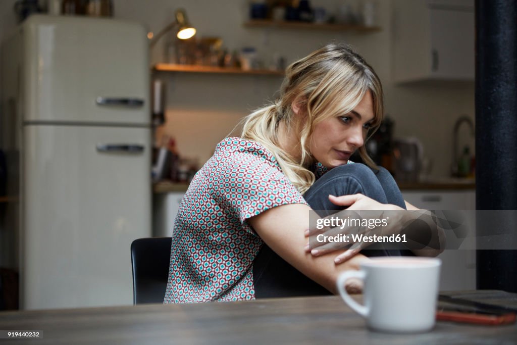 Portrait of pensive woman sitting at table in the kitchen