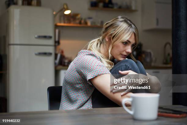 portrait of pensive woman sitting at table in the kitchen - triste imagens e fotografias de stock