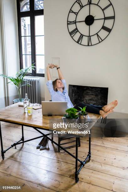 relaxed woman sitting at desk at home with feet up - clock person desk stockfoto's en -beelden