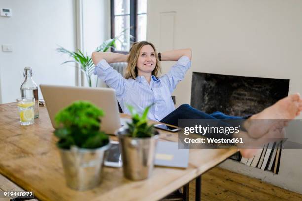 smiling woman sitting at desk at home with feet up - feet on desk stock pictures, royalty-free photos & images