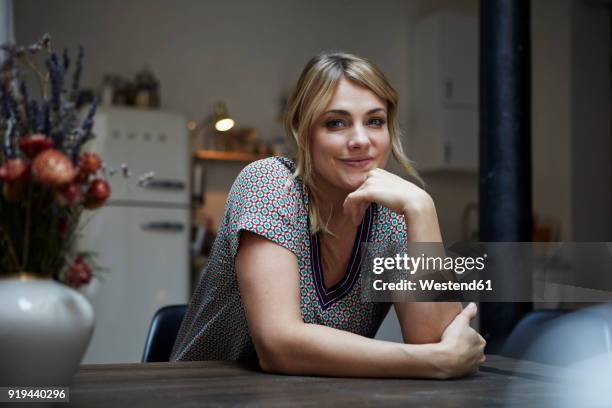 portrait of smiling woman sitting at table in the kitchen - sitting at table looking at camera stock-fotos und bilder