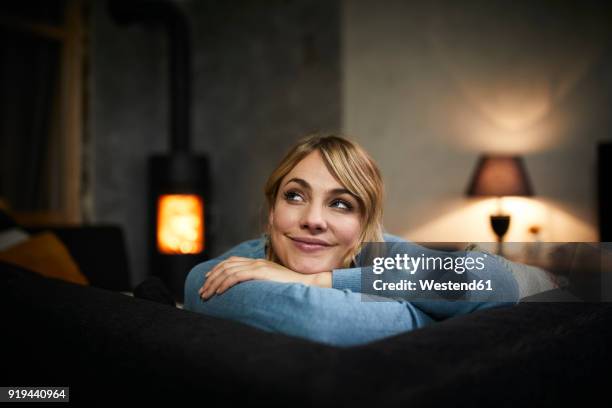 portrait of smiling woman relaxing on couch at home in the evening - fireplace imagens e fotografias de stock