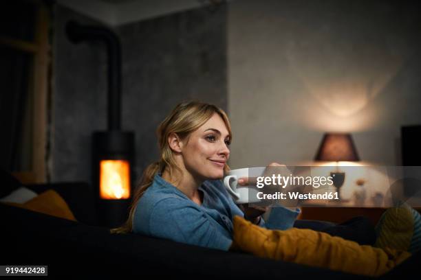 portrait of happy woman with cup of tea relaxing on couch at home in the evening - hot blondes images stock pictures, royalty-free photos & images