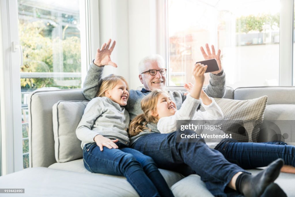 Two happy girls and grandfather on sofa taking a selfie