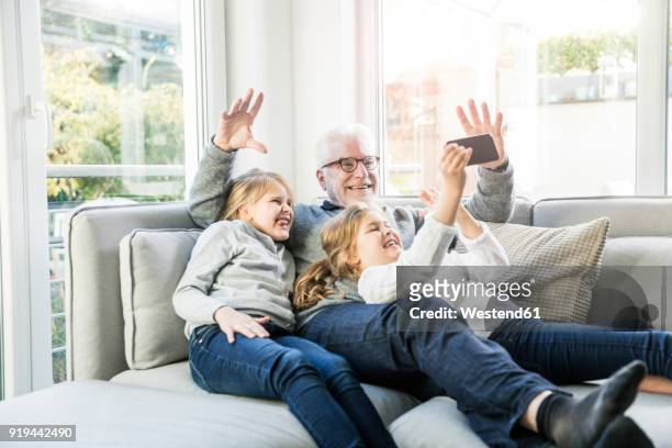 two happy girls and grandfather on sofa taking a selfie - photo call stock-fotos und bilder