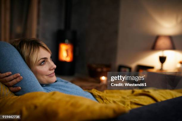 smiling woman relaxing on couch at home in the evening - open fire stock pictures, royalty-free photos & images