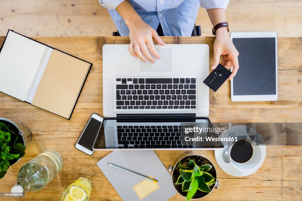 Top view of woman at wooden desk with credit card and laptop