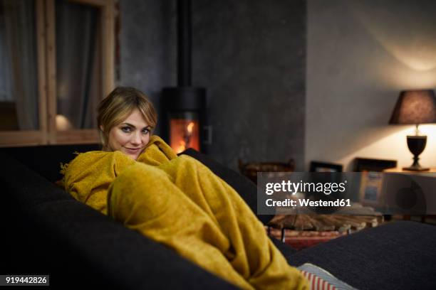 portrait of smiling woman relaxing on couch at home in the evening - wrapped in a blanket stock pictures, royalty-free photos & images