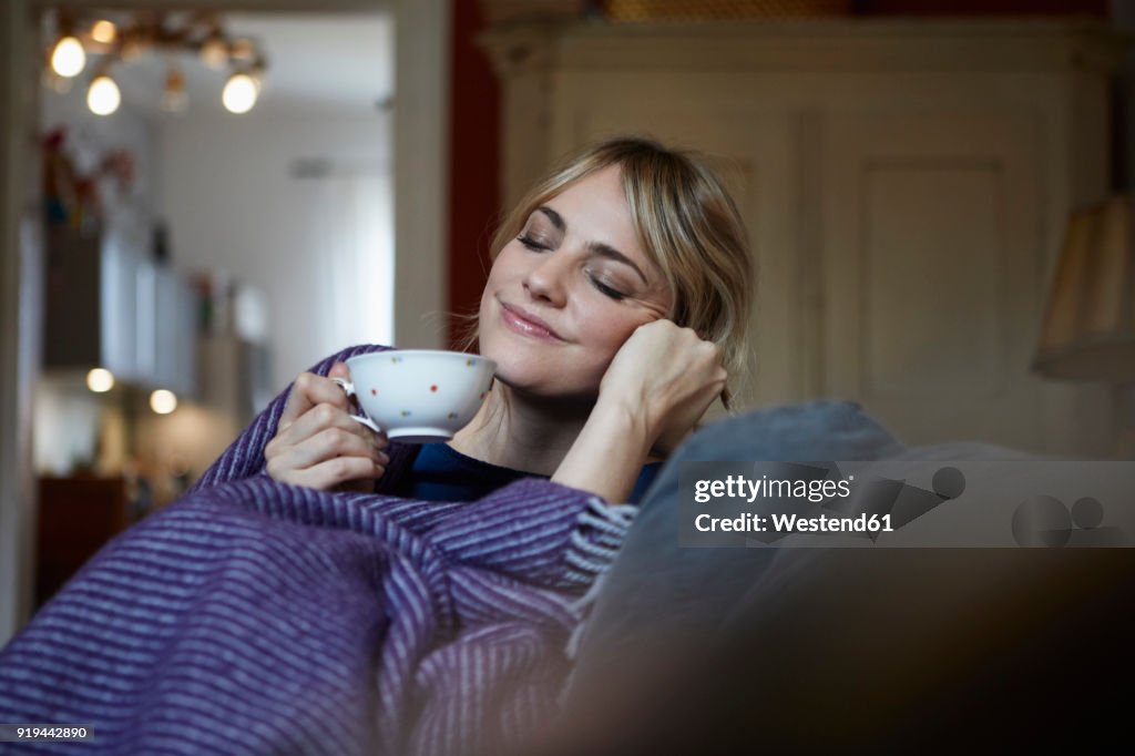 Portrait of smiling woman with cup of tea relaxing on couch at home