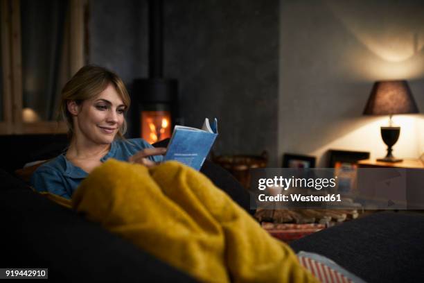 portrait of smiling woman reading a book on couch at home in the evening - reading ストックフォトと画像