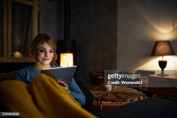 portrait of smiling woman with tablet relaxing on couch in the evening - abenddämmerung stock-fotos und bilder