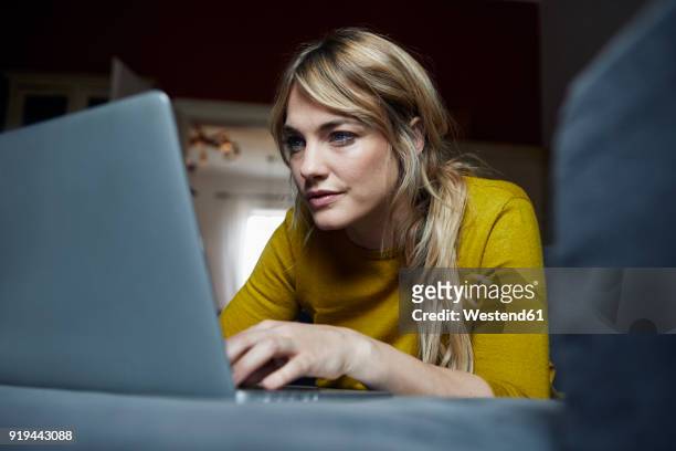 portrait of woman lying on the couch at home using laptop - concentration stock pictures, royalty-free photos & images