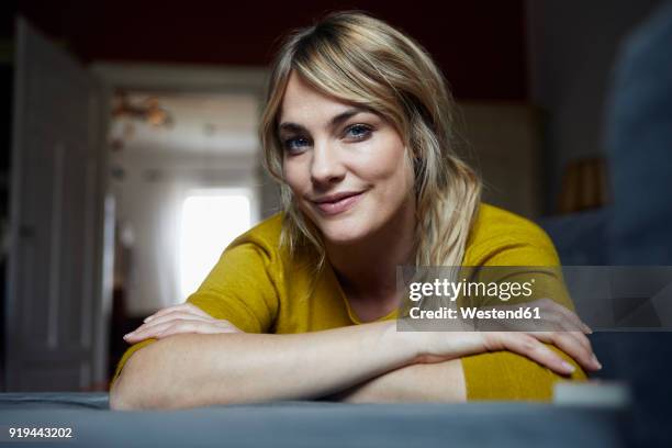 portrait of smiling woman relaxing on the couch at home - looking at camera stock-fotos und bilder