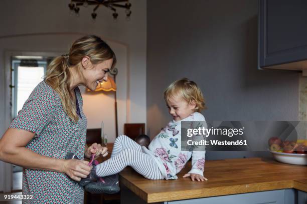 mother tying shoe of her little daughter in the kitchen - family shoes stock-fotos und bilder