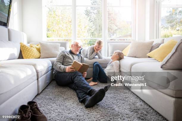 two girls and grandfather reading book in living room - espacio confortable fotografías e imágenes de stock