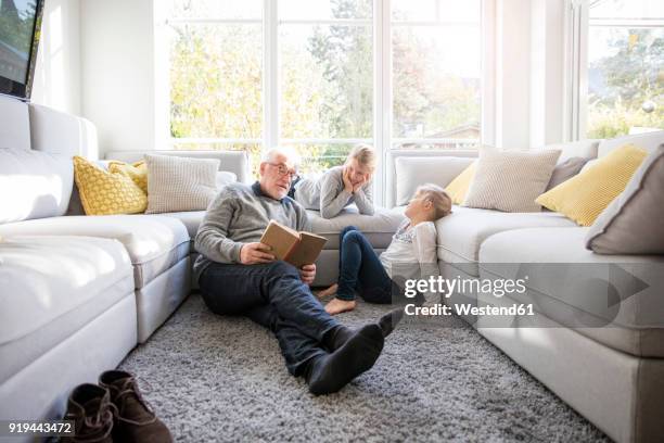 two girls and grandfather reading book in living room - kids hobbies stock pictures, royalty-free photos & images