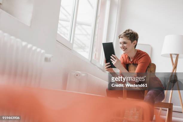 smiling woman sitting on chair using tablet - selective focus stock-fotos und bilder