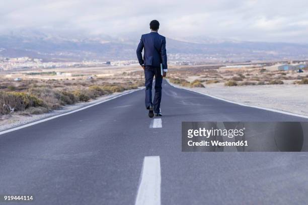 spain, tenerife, young businessman with laptop walking on road - 後ろ姿　男性 ストックフォトと画像