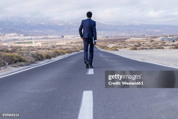 spain, tenerife, young businessman with laptop walking on road - origins imagens e fotografias de stock