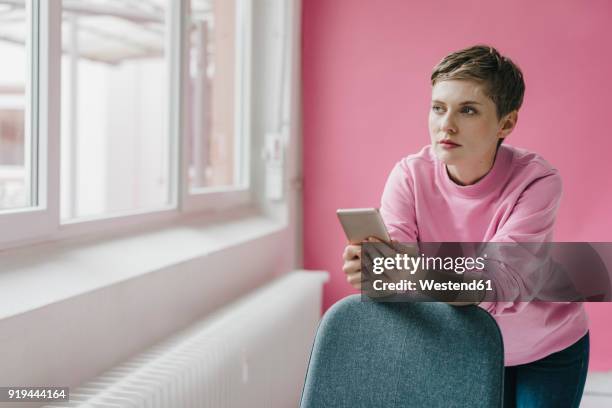 pensive woman with cell phone looking out of window - 30 34 jaar stockfoto's en -beelden