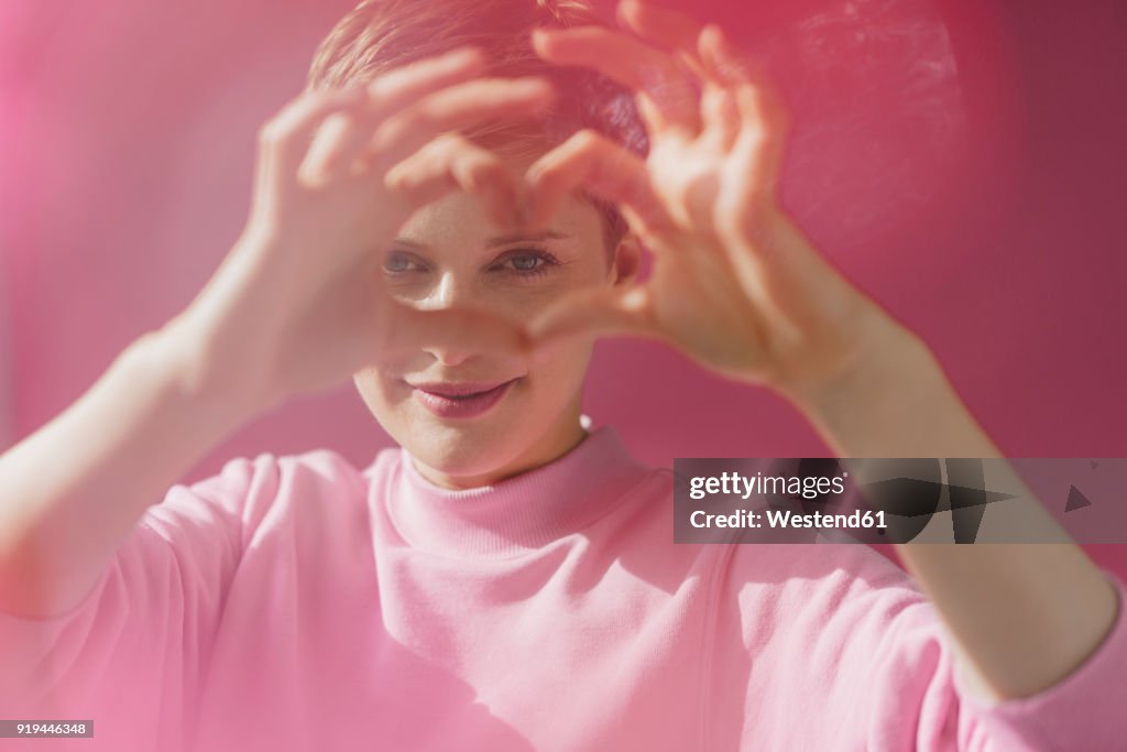 Portrait of woman in pink shaping heart with her hands