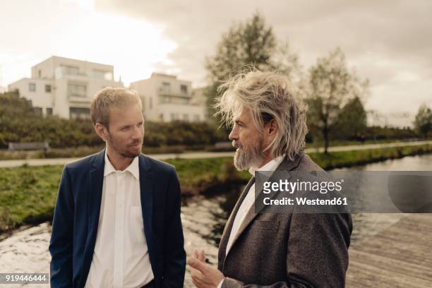 two businessmen talking at a lake - father son business europe stock-fotos und bilder