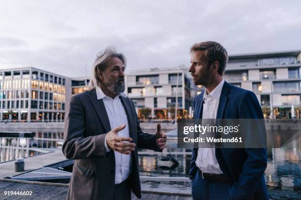 two businessmen talking at city harbor at dusk - business man standing stock-fotos und bilder