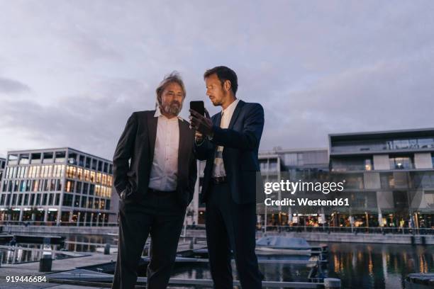 two businessmen with cell phone at city harbor at dusk - dortmund city centre stock pictures, royalty-free photos & images