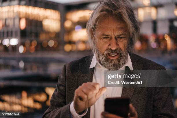 senior man using cell phone outdoors at dusk - portrait of business man looking surprised stock-fotos und bilder