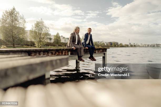 two businessmen sitting on jetty at a lake - father and son discussion ストックフォトと画像
