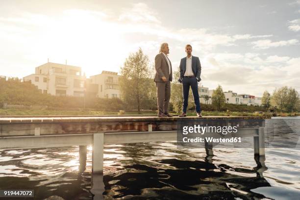 two businessmen standing on jetty at a lake - holzsteg stock-fotos und bilder