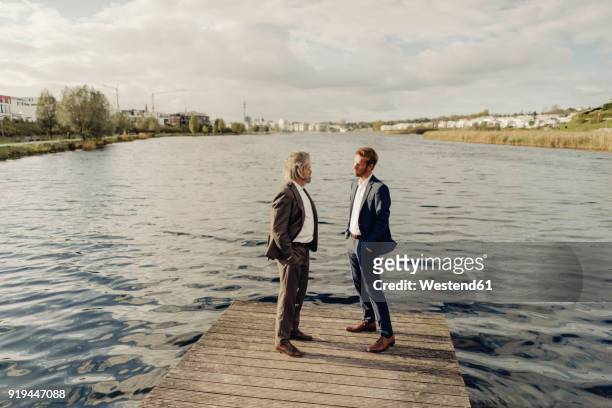 two businessmen standing on jetty at a lake talking - father son business europe stock-fotos und bilder