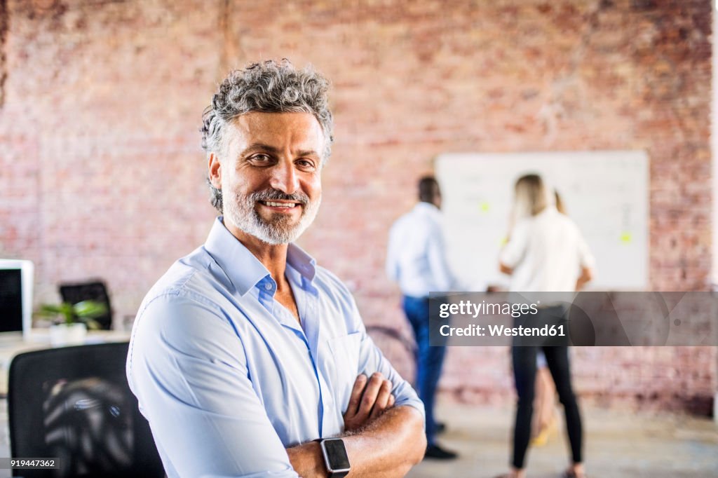 Portrait of smiling businessman in office with colleagues in background