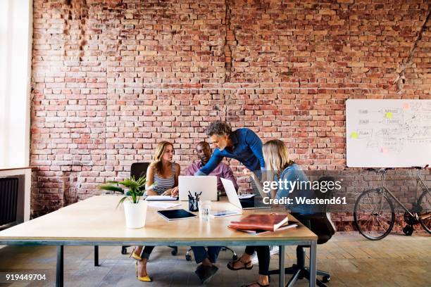 business people with laptops discussing at desk in office - loft brique photos et images de collection
