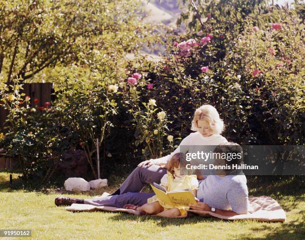 Family of three reading on lawn in park