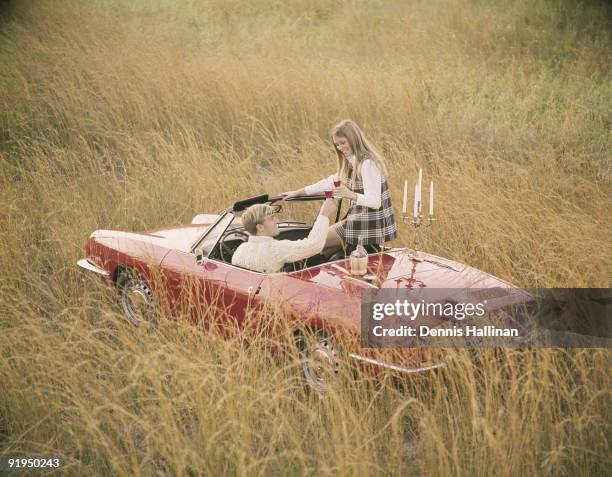 Romantic couple in sports car convertible enjoying wine in field