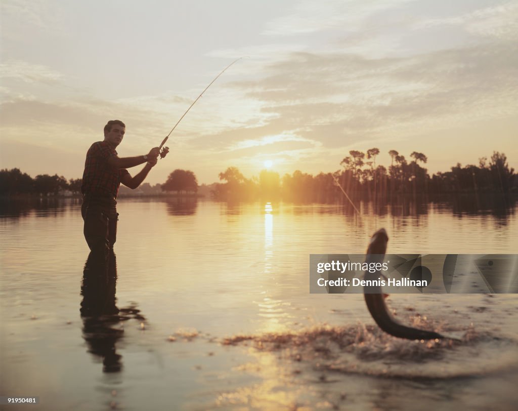 Man catching fish in lake at sunset
