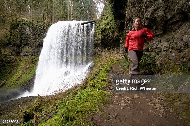 a woman trail running next to a waterfall in silver falls state park, oregon, usa. - salem oregon fotografías e imágenes de stock
