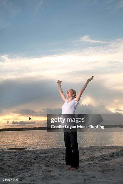 a pregnant woman stands on a beach at sunset and raises her arms towards the sky. - ライツヴィルビーチ ストックフォトと画像