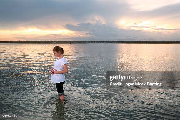 a pregnant woman stands in a calm ocean at sunset. - ライツヴィルビーチ ストックフォトと画像